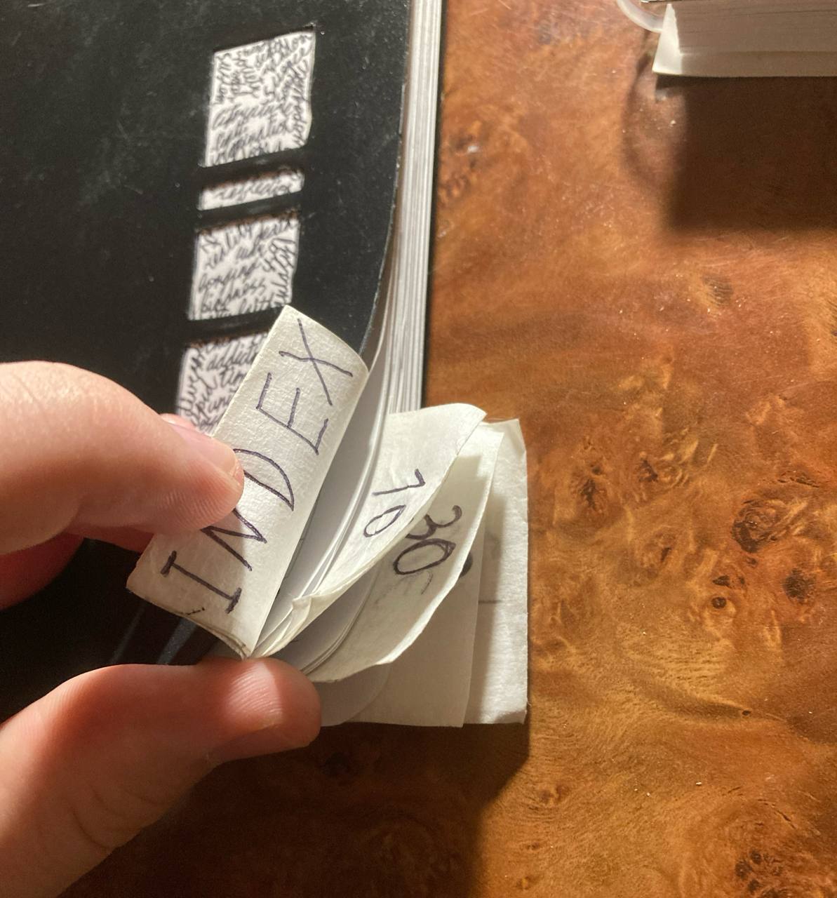 Corner of the Commonplace. A hand is holding the tabs protruding from the bottom. The visible tabs are “INDEX,” page 10, and page 30. All of them are made from paper tape with an office paper insert for readability.